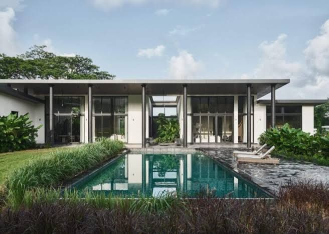 Modern house with large windows, surrounded by greenery, and a reflective swimming pool in the foreground.
